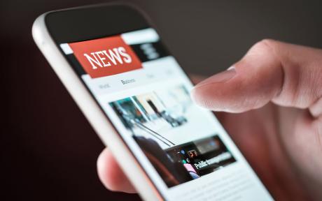 Close up of a person's thumb scrolling through the news on their phone.
